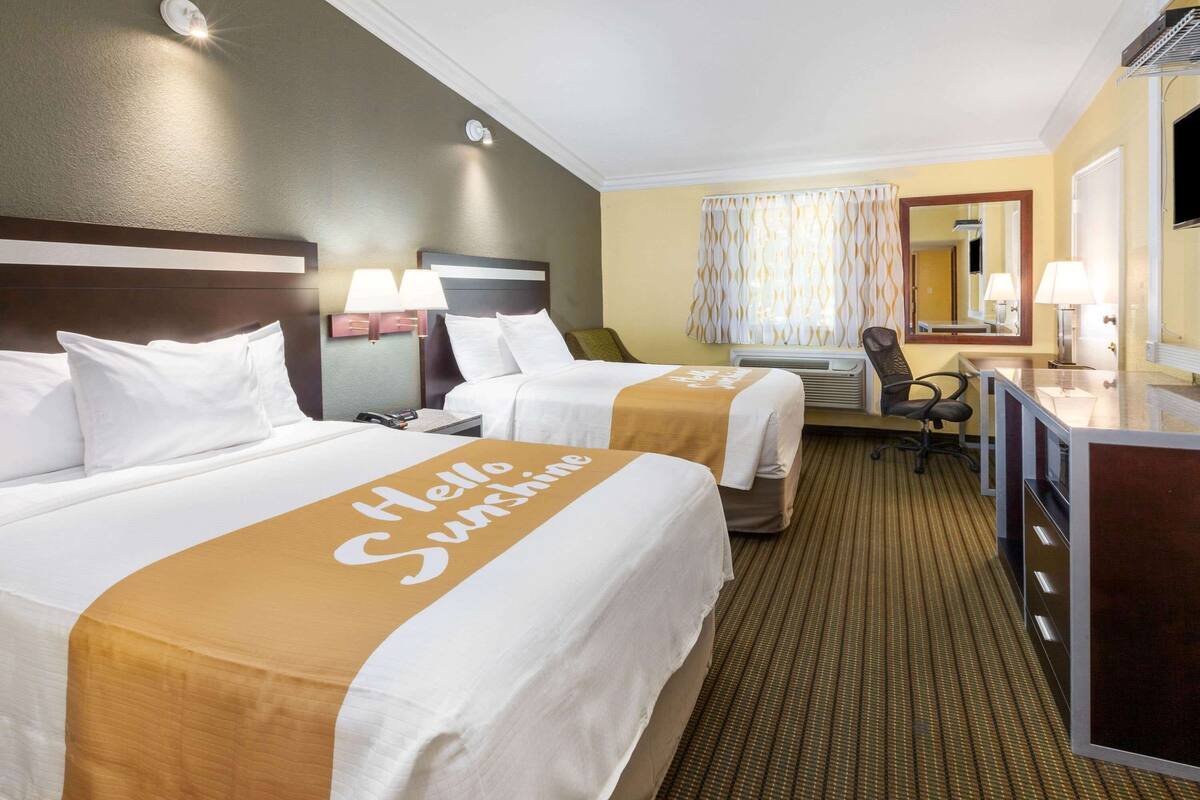 A hotel room with two beds, a desk, and a chair.