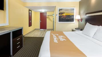 A hotel room with a bed, a desk, a mirror, a door, and a painting on the wall.