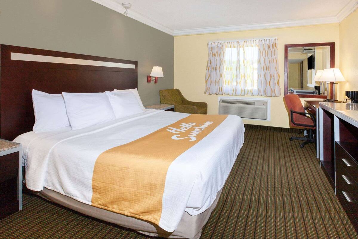 A hotel room with a bed, a desk, a chair, a mirror, and a window with curtains.