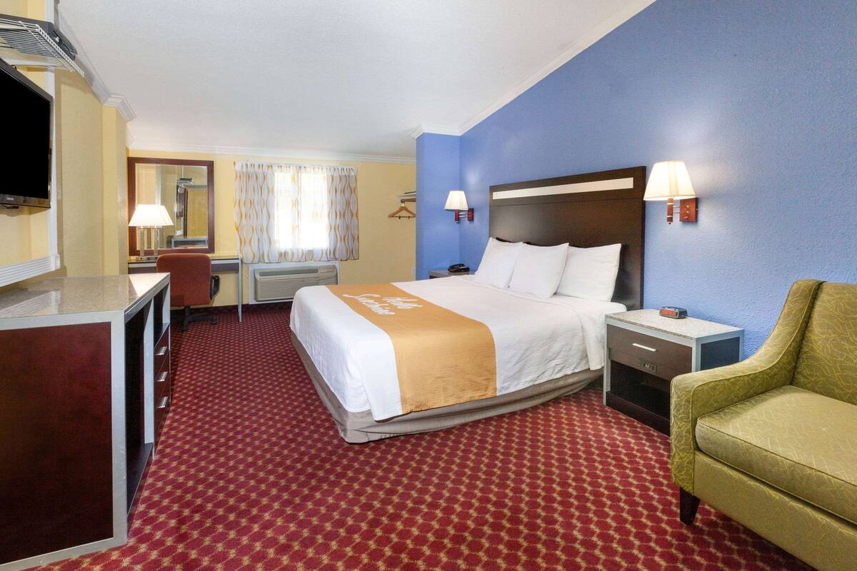 A hotel room with a bed, a desk, a chair, a TV, and a lamp.