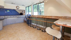 A Days Inn reception area with a counter, bar stools, and a clock on the wall. - Days Inn by Wyndham Nanuet / Spring Valley (Nanuet)
