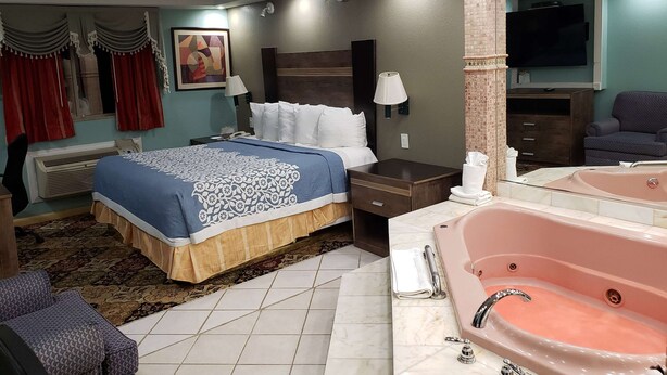 A hotel room with a large bed, a sitting area with a chair, a bathroom with a bathtub, and a television on the wall. - Days Inn by Wyndham Nanuet / Spring Valley (Nanuet)