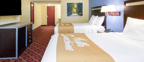 Habitación de hotel con dos camas, un televisor, un microondas, un cuadro de un bosque y un corredor de cama con el texto 'Hello Sunshine'.