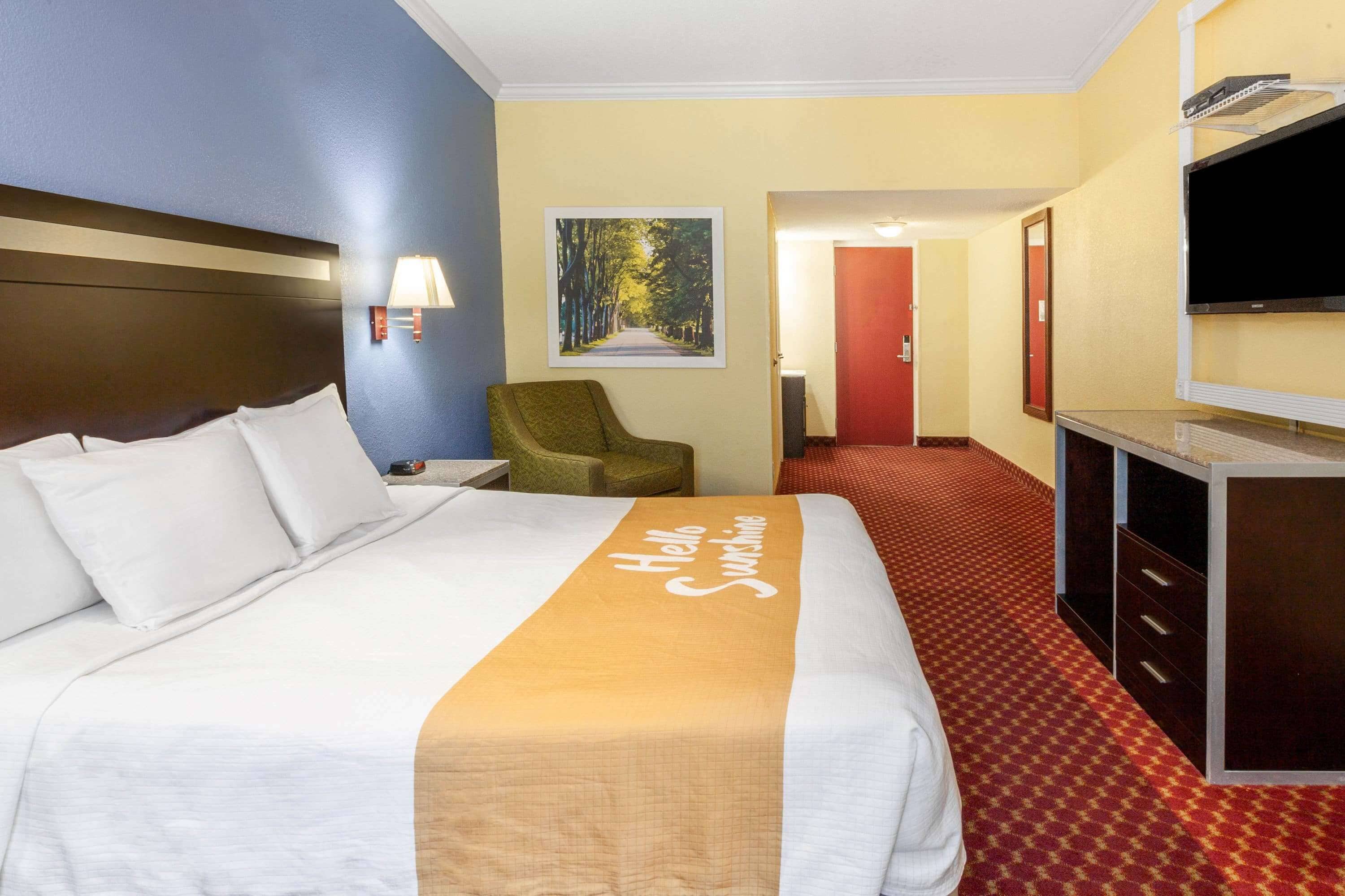 A hotel room with a large bed, a desk, a chair, a TV, and a painting on the wall.