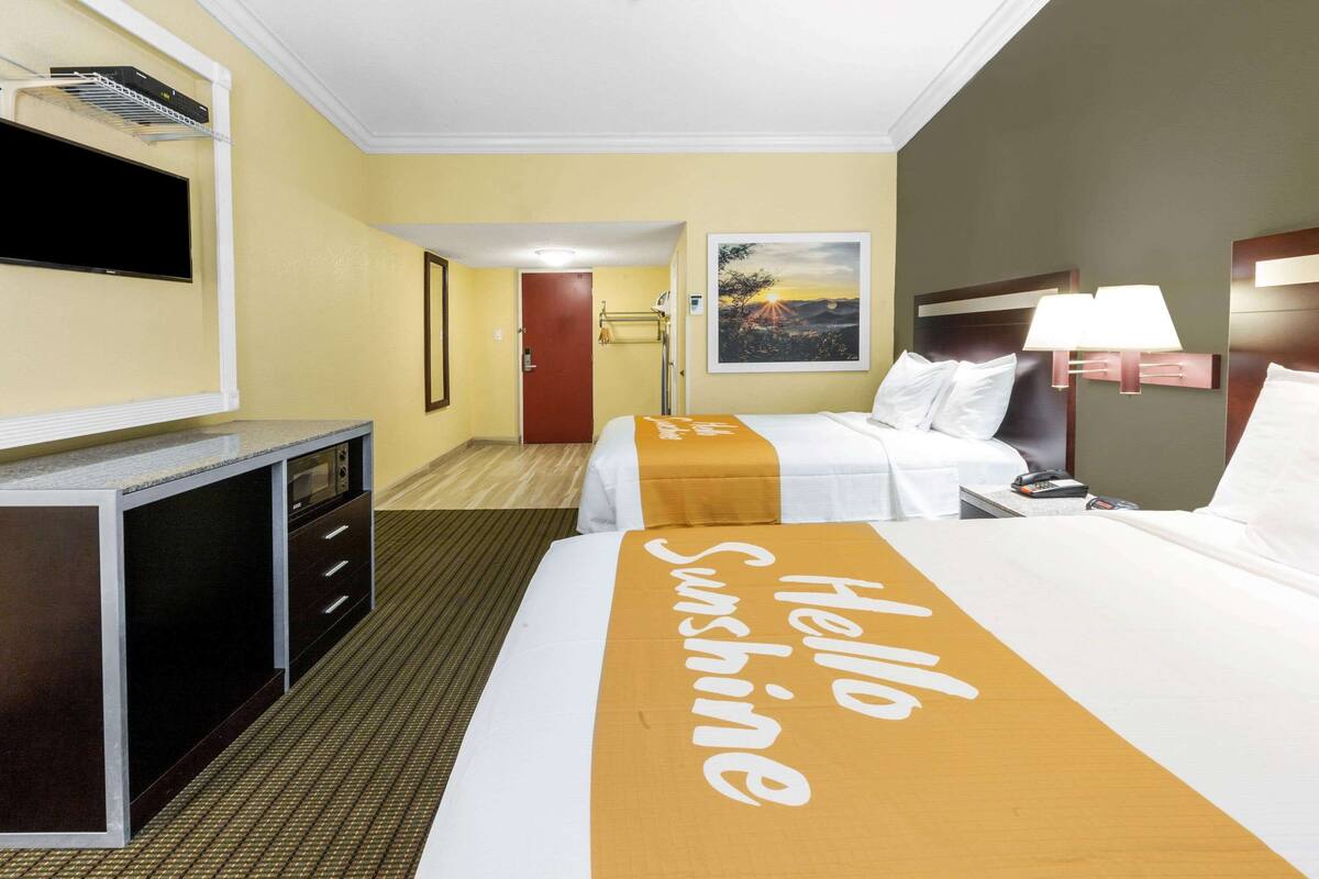 A hotel room with a bed, a desk, a television, and a painting on the wall.