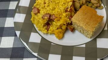 A plate of food with rice, beans, and cornbread on a checkered tablecloth.