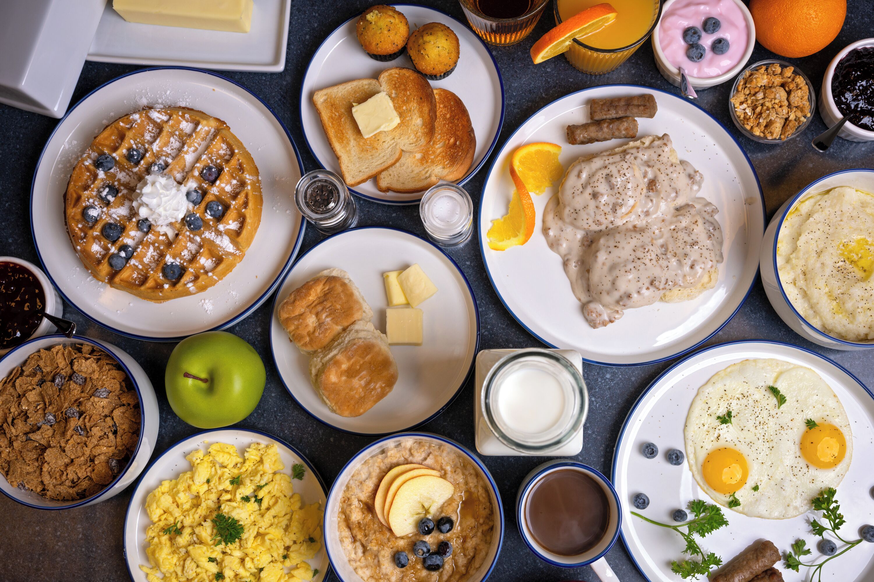 Een ontbijttafel met diverse gerechten, waaronder wafels, toast, roerei en havermout.
