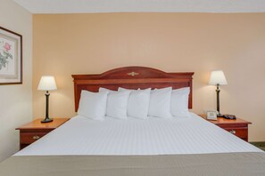 A neatly made bed with white linens, two bedside tables with lamps, and a wooden headboard. - Days Inn by Wyndham Asheville West (Candler)