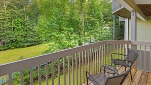 Une terrasse en bois avec deux chaises et une table, offrant une vue sur un paysage verdoyant et luxuriant, parsemé d’arbres.