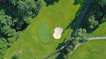 An aerial view of a golf course with a sand bunker, a putting green, and a curved pathway.