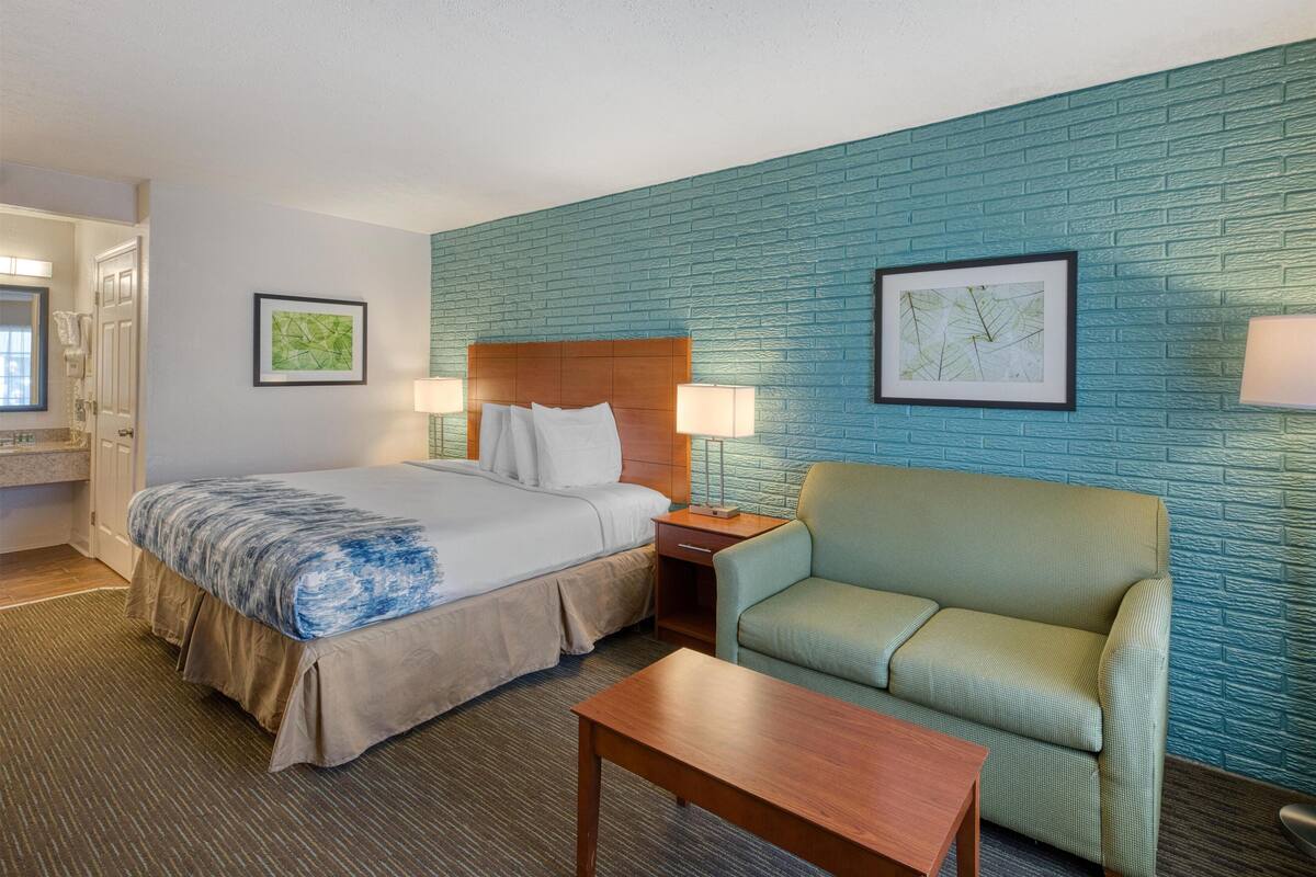 A hotel room with a bed, a green armchair, a wooden nightstand, and two wall-mounted lamps.