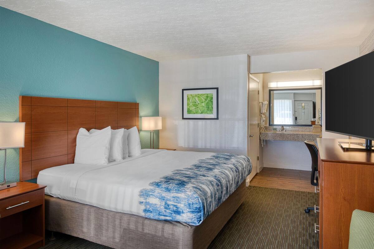 A hotel room with a bed, a desk, a chair, a television, and a bathroom visible through an open door.