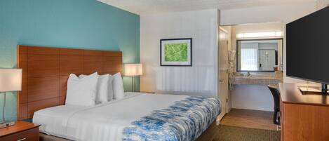 Habitación de hotel con cama, escritorio, silla, televisión y baño visible a través de una puerta abierta.