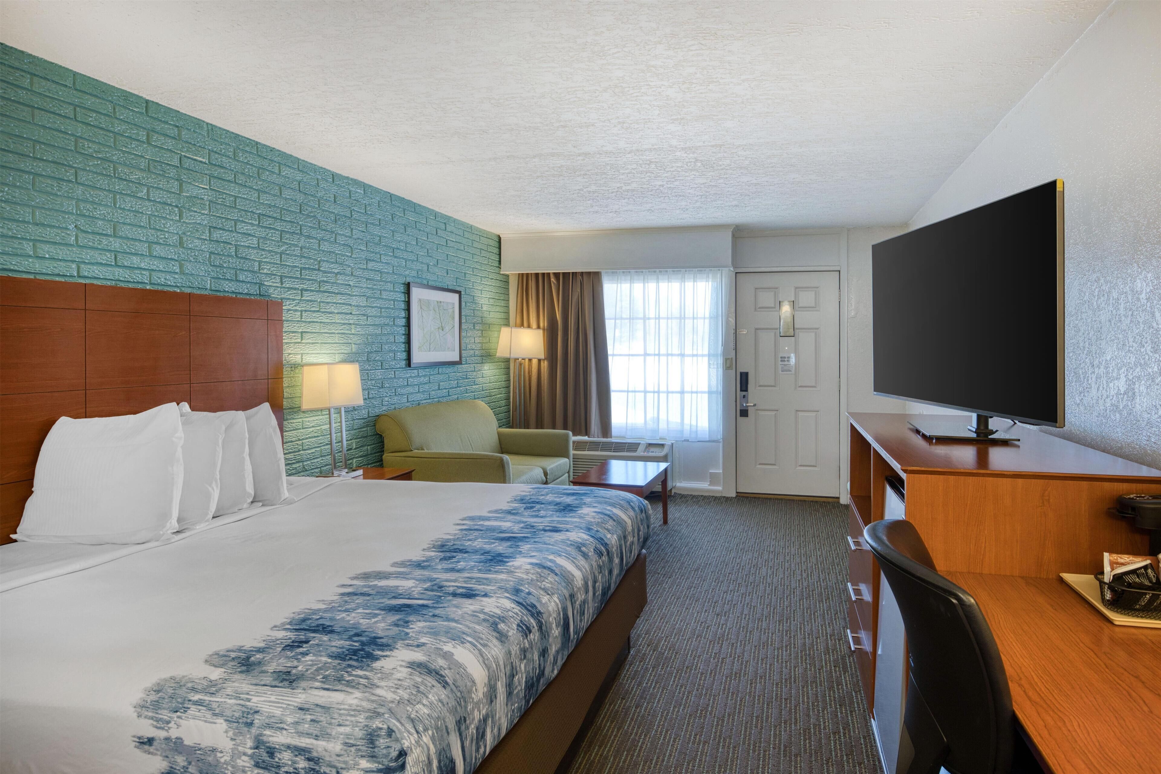 A hotel room with a large bed, a desk, a television, a chair, and a window with curtains.