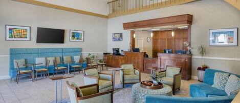 A spacious lobby with a high ceiling, a reception desk, seating areas, and artwork on the walls.