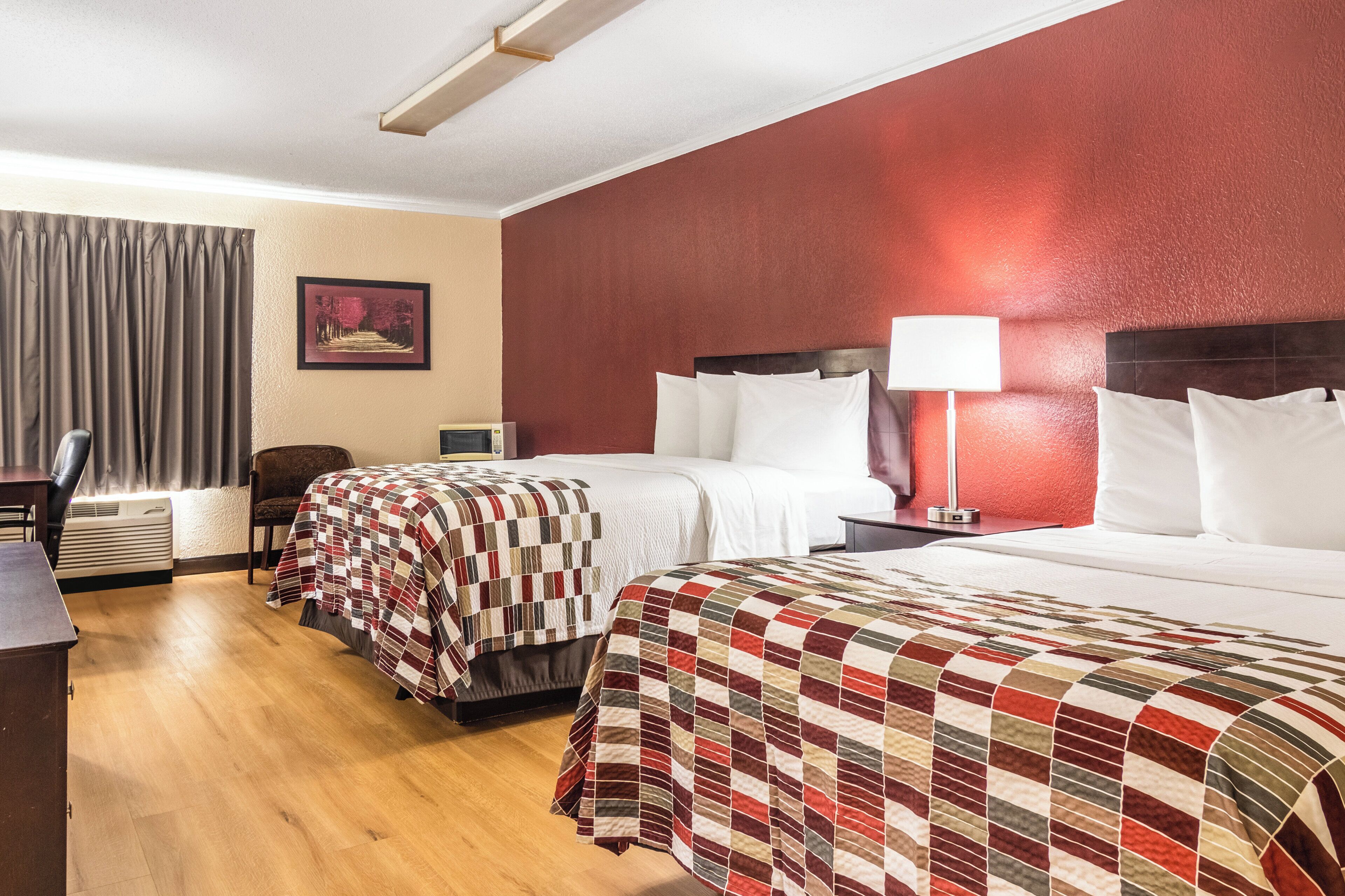 A hotel room with two beds, a desk, a chair, a lamp, and a painting on the wall.