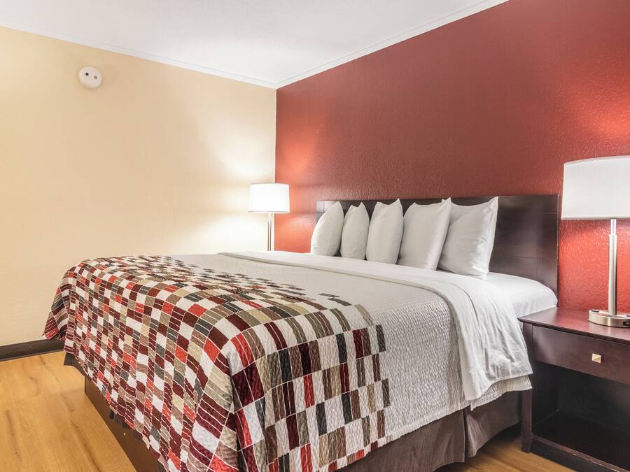Una habitación de hotel con cama, mesita de noche, lámpara y pared con textura.