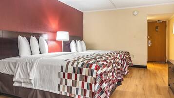 Habitación de hotel con una cama grande, una lámpara de noche, suelo de madera y una puerta a la derecha.