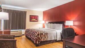 A hotel room with a bed, a desk, a chair, a window with curtains, an air conditioner, and a wall-mounted picture. - Red Roof Inn Ashtabula - Austinburg (Austinburg)