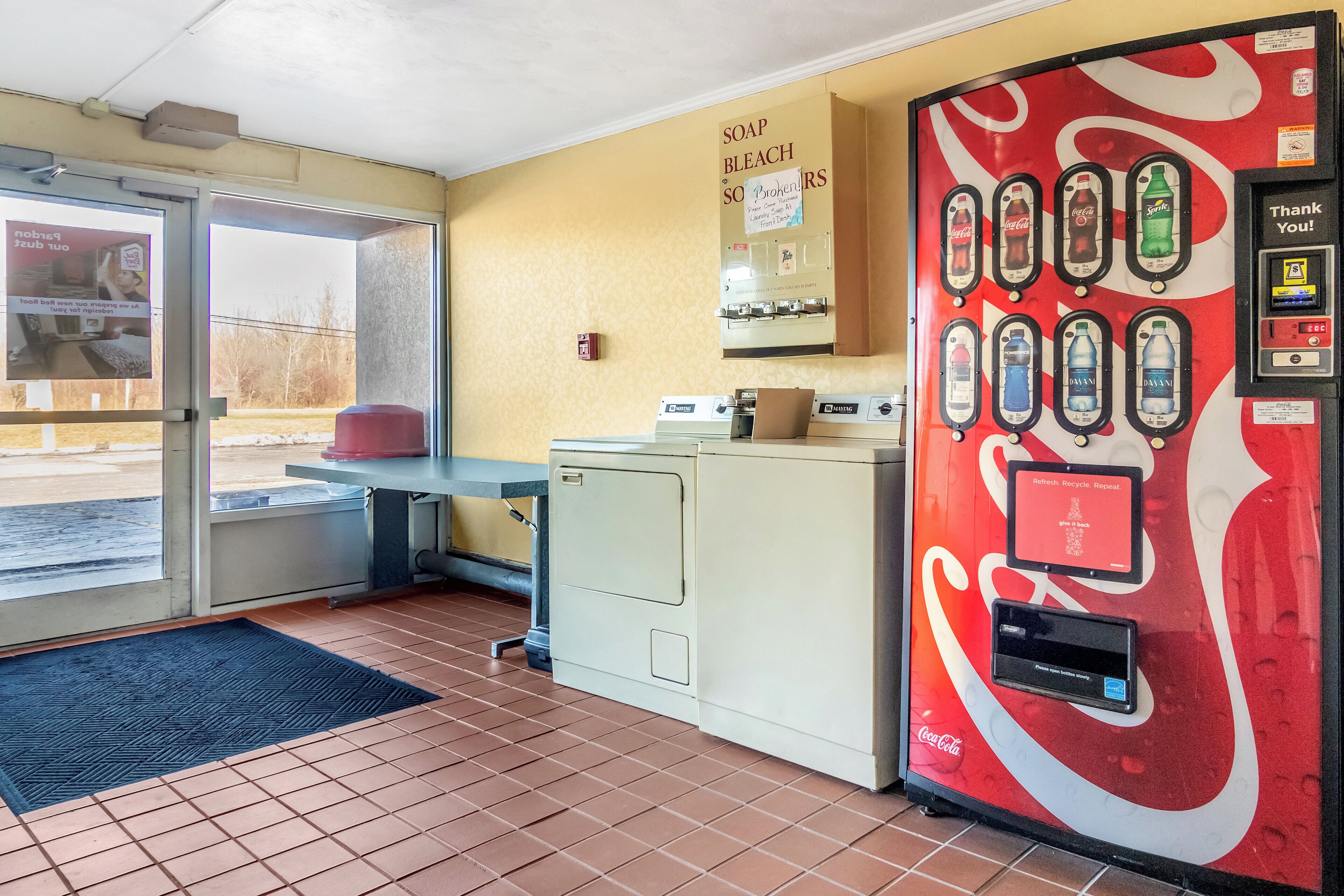 A room with a vending machine, a door, a window, and a tiled floor.