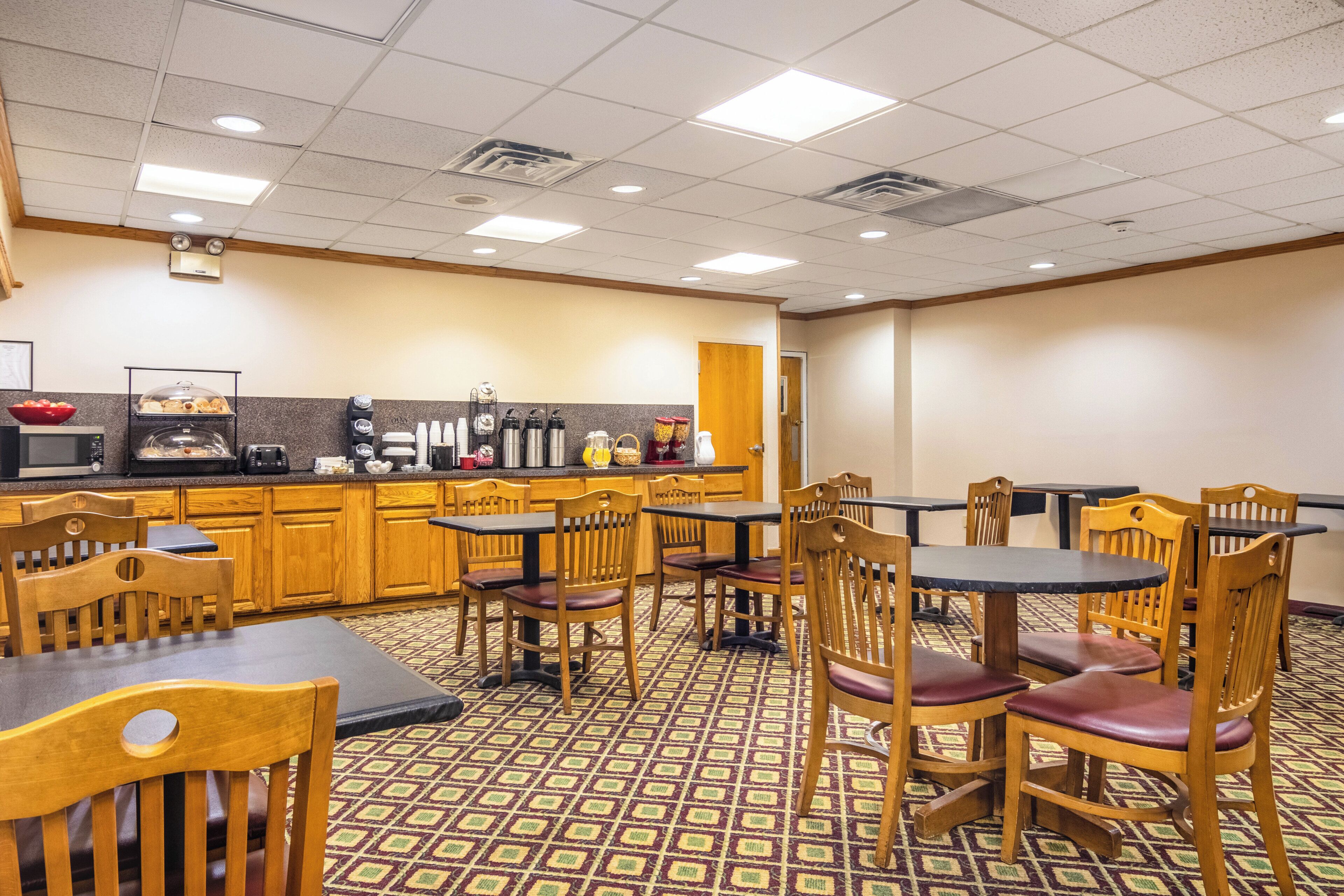 A dining area with wooden chairs and tables, a kitchen counter with appliances, and patterned flooring.