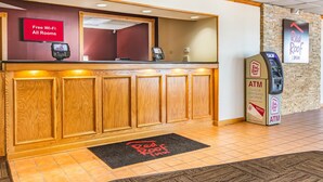 A reception desk with a Red Roof Inn sign, an ATM, and a Red Roof Inn logo on the floor mat. - Red Roof Inn Ashtabula - Austinburg (Austinburg)