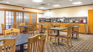 A dining area with wooden tables and chairs, a kitchen counter with appliances, and a patterned floor. - Red Roof Inn Ashtabula - Austinburg (Austinburg)