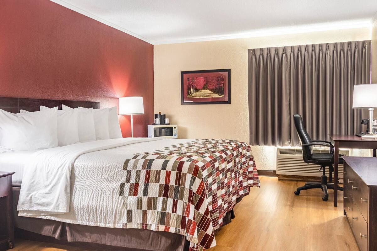 A hotel room with a bed, desk, chair, lamp, and a picture on the wall.