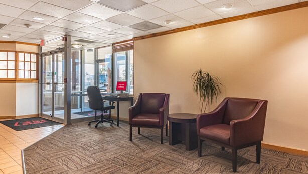 A lobby with a reception desk, two leather chairs, a potted plant, and a patterned carpet. - Red Roof Inn Ashtabula - Austinburg (Austinburg)