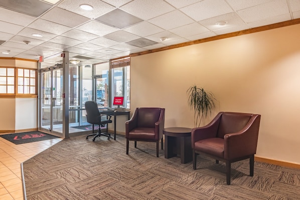 A lobby with a reception desk, two leather chairs, a potted plant, and a patterned carpet.