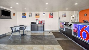 A hotel lobby with a reception desk, a kitchenette, and a seating area with chairs and a table.