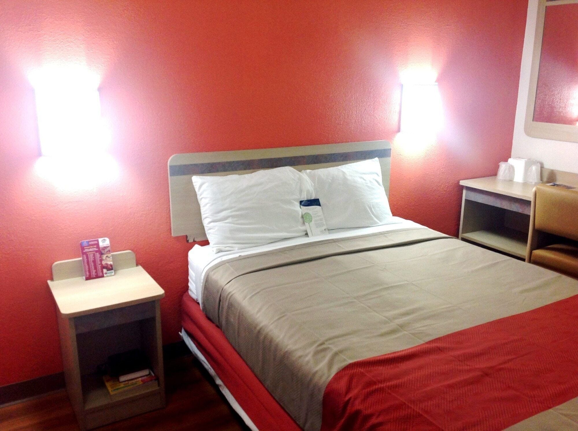 A hotel room with a single bed, a nightstand, a red wall, and a small table with toiletries.