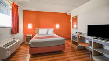 A hotel room with a bed, a desk with a chair, a television, and a heater.
