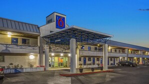 A motel with a prominent '6' sign, a covered parking area, and multiple rooms with visible windows.