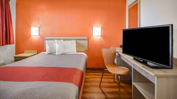 A hotel room with a bed, a desk with a television, and two wall-mounted lights.