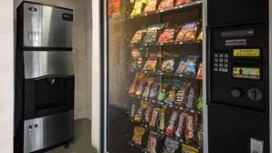 A vending machine stocked with various snacks and a stainless steel refrigerator.