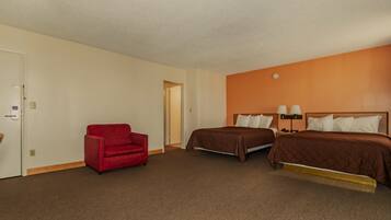 A hotel room with two beds, a red armchair, and a door.