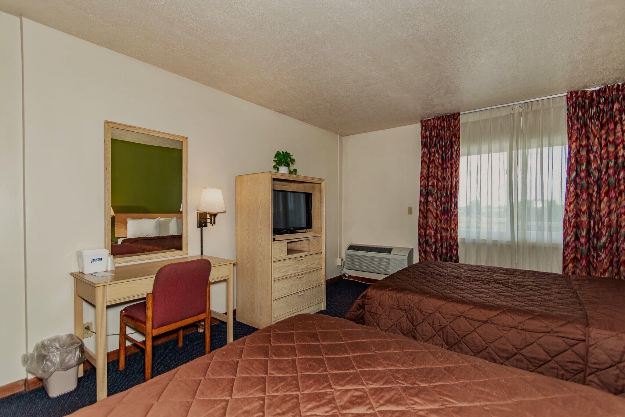 Une chambre d’hôtel comprenant un lit, un bureau avec une chaise, une télévision, un miroir et une fenêtre avec des rideaux.