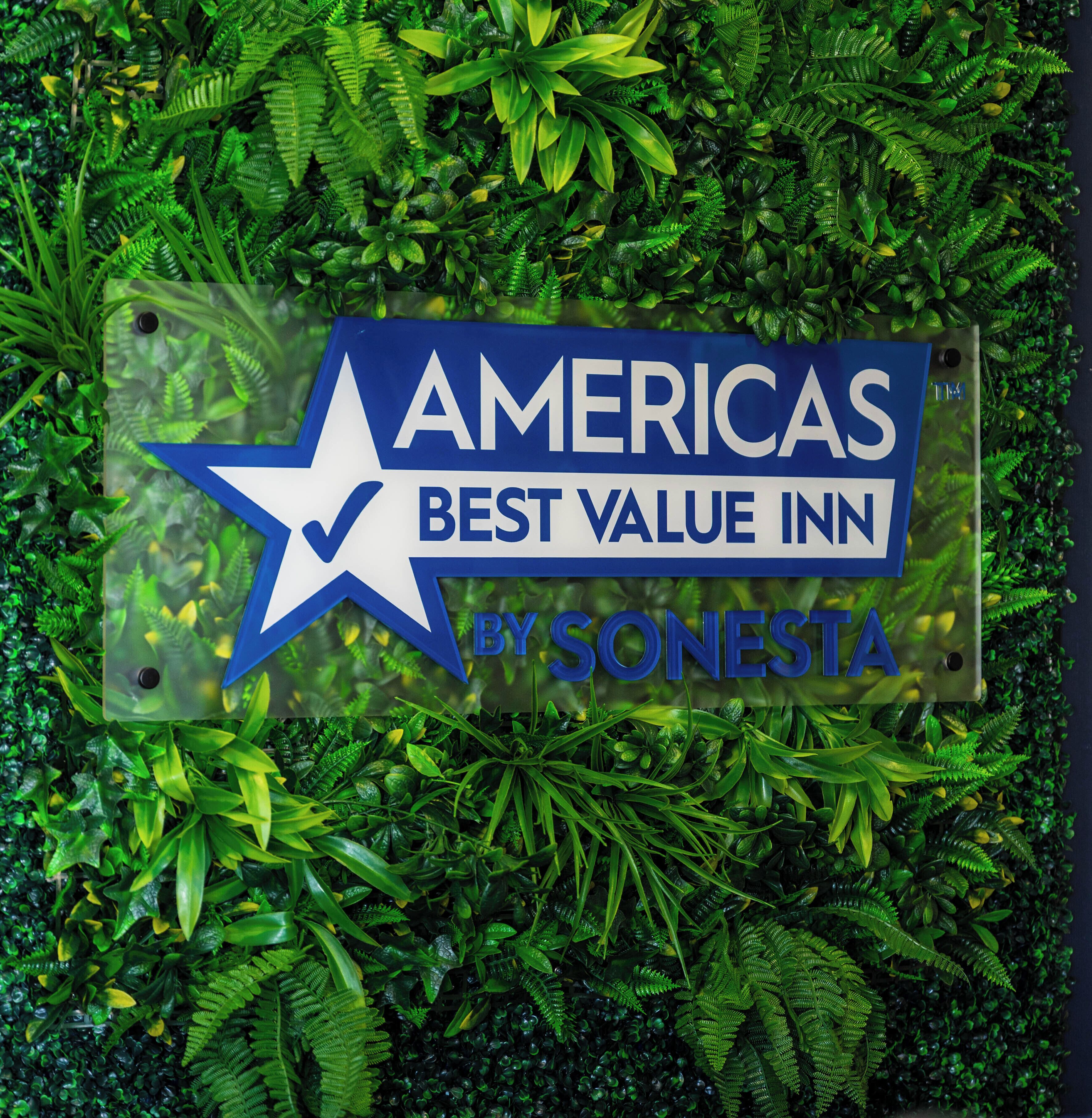 A sign for 'AMERICAS BEST VALUE INN' by SONESTA against a backdrop of green foliage.
