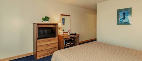 A bedroom with a bed, a wooden dresser with a television, a desk with a chair, and a wall-mounted painting.