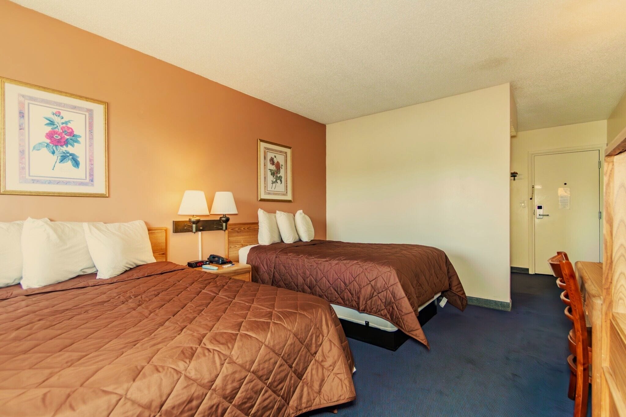 A hotel room with two beds, a nightstand, a lamp, and a door leading to a bathroom.