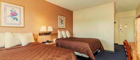 A hotel room with two beds, a nightstand, a lamp, and a door leading to a bathroom.