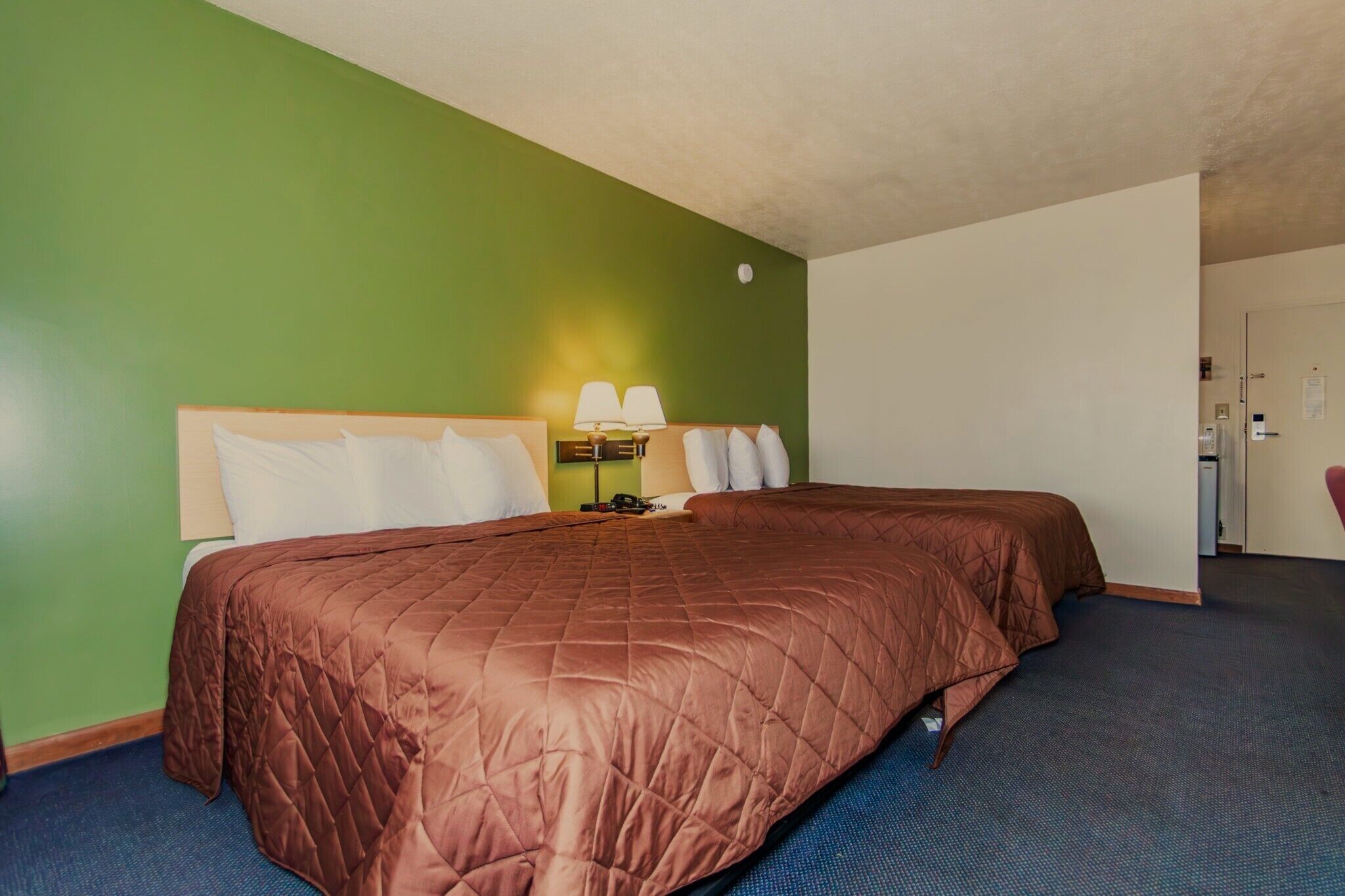 A hotel room with a large bed, a desk with a lamp, and a chair.