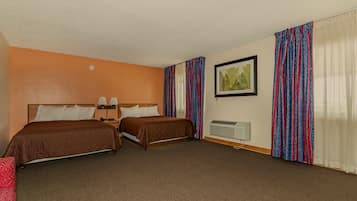 Ein Hotelzimmer mit zwei Betten, einem Einzelbett, einem Nachttisch, einer Lampe, einem gerahmten Bild und einem Fenster mit gemusterten Vorhängen.
