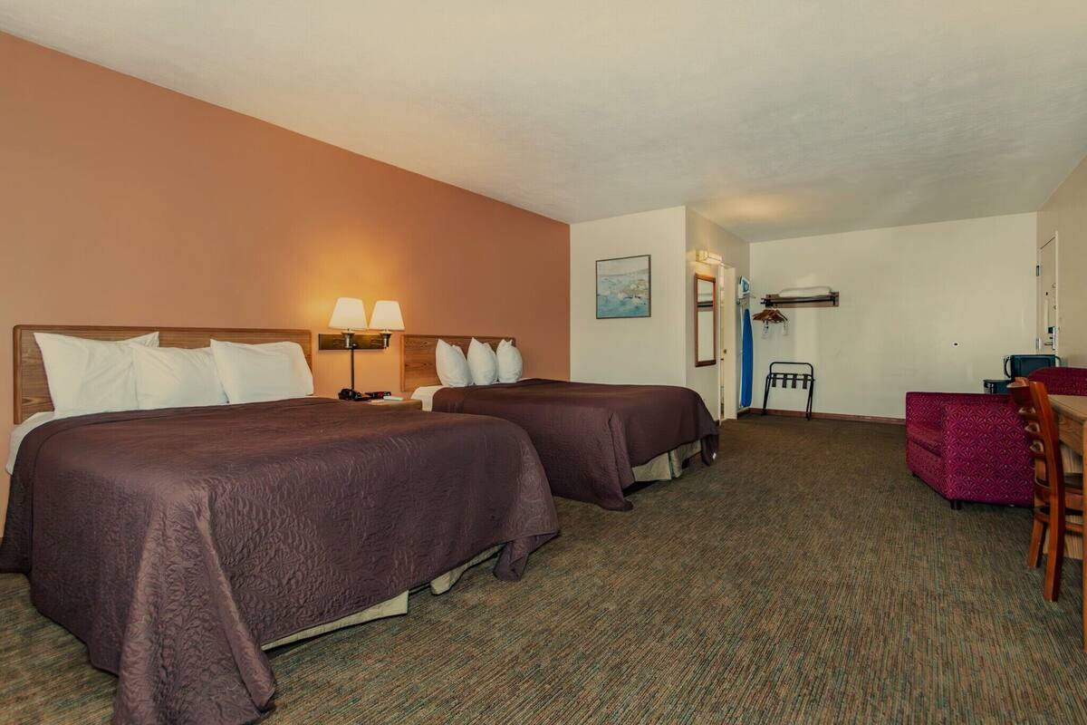 A hotel room with two beds, a desk, a chair, and a small table.