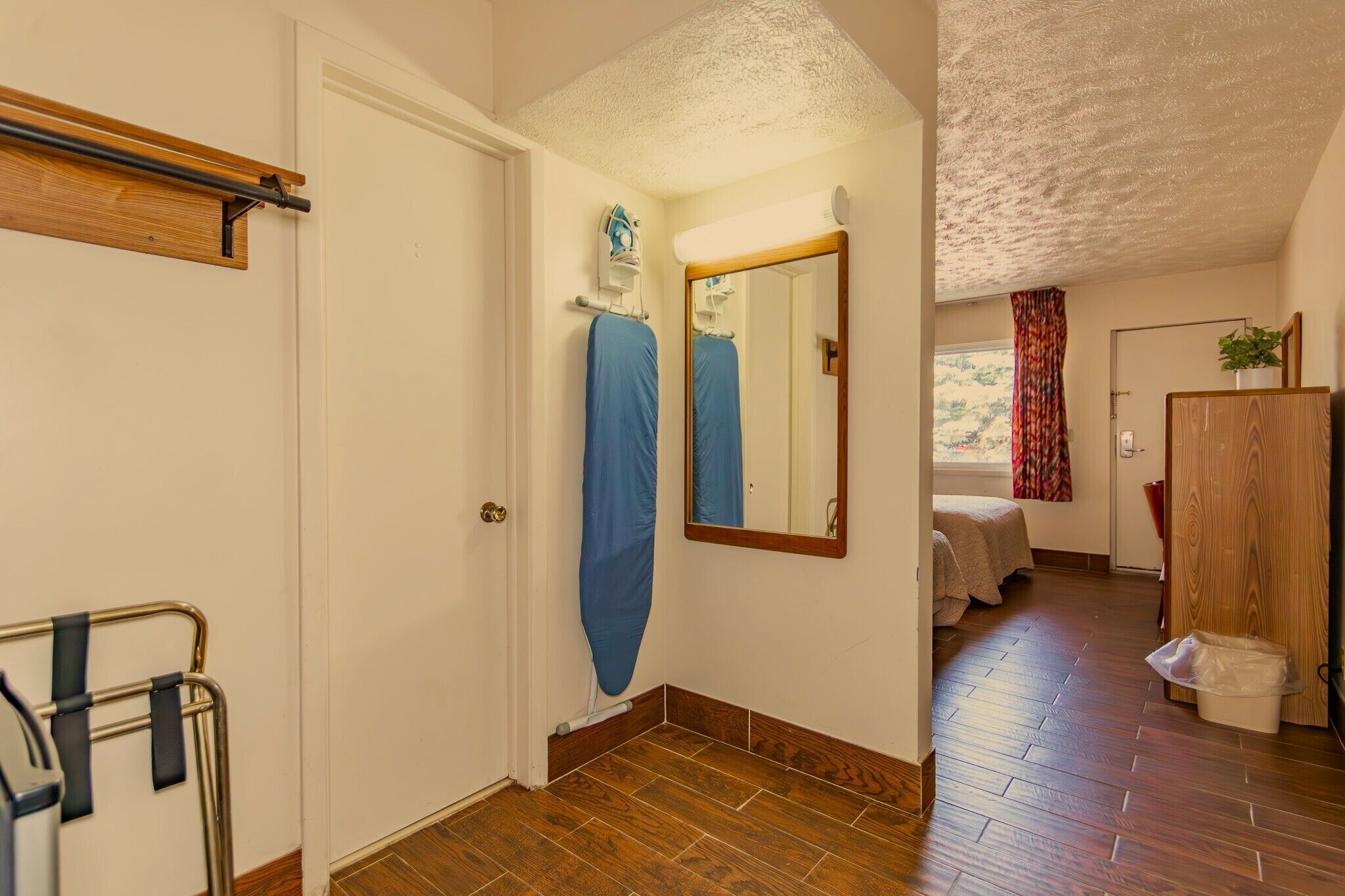 Un corridoio con pavimento in legno, una porta, uno specchio e un letto sullo sfondo.