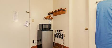 A compact room with a refrigerator, microwave, and a clothes drying rack.