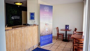 Un'area reception di un hotel con una scrivania di legno, un poster Sonesta per viaggi, un monitor per computer e una sala da pranzo con sedie e tavoli di legno.
