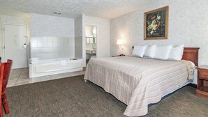 Camera d'albergo con un letto grande, bagno separato con vasca, doccia e una piccola area salotto con una sedia.