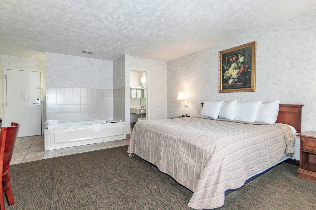 A hotel room with a large bed, a separate bathroom with a bathtub, a shower, and a small seating area with a chair.